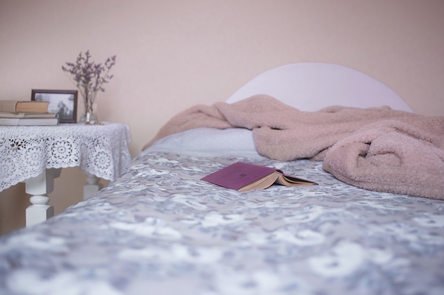 postel s hnědým přehozem, stolkem a fialovou knihou